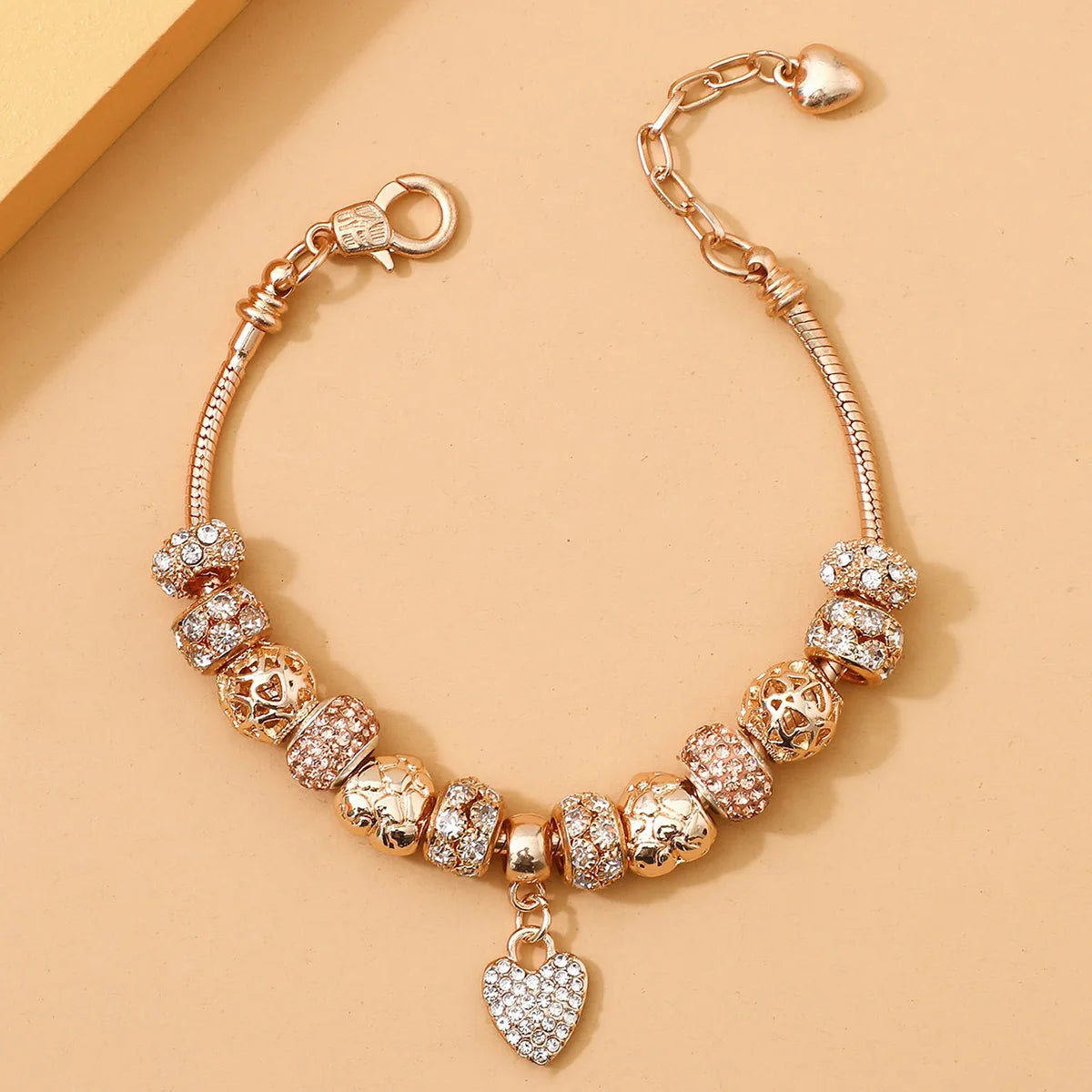 Rose gold charm bracelet by Tidesmit, featuring crystal-studded beads and a central heart charm on a snake chain.