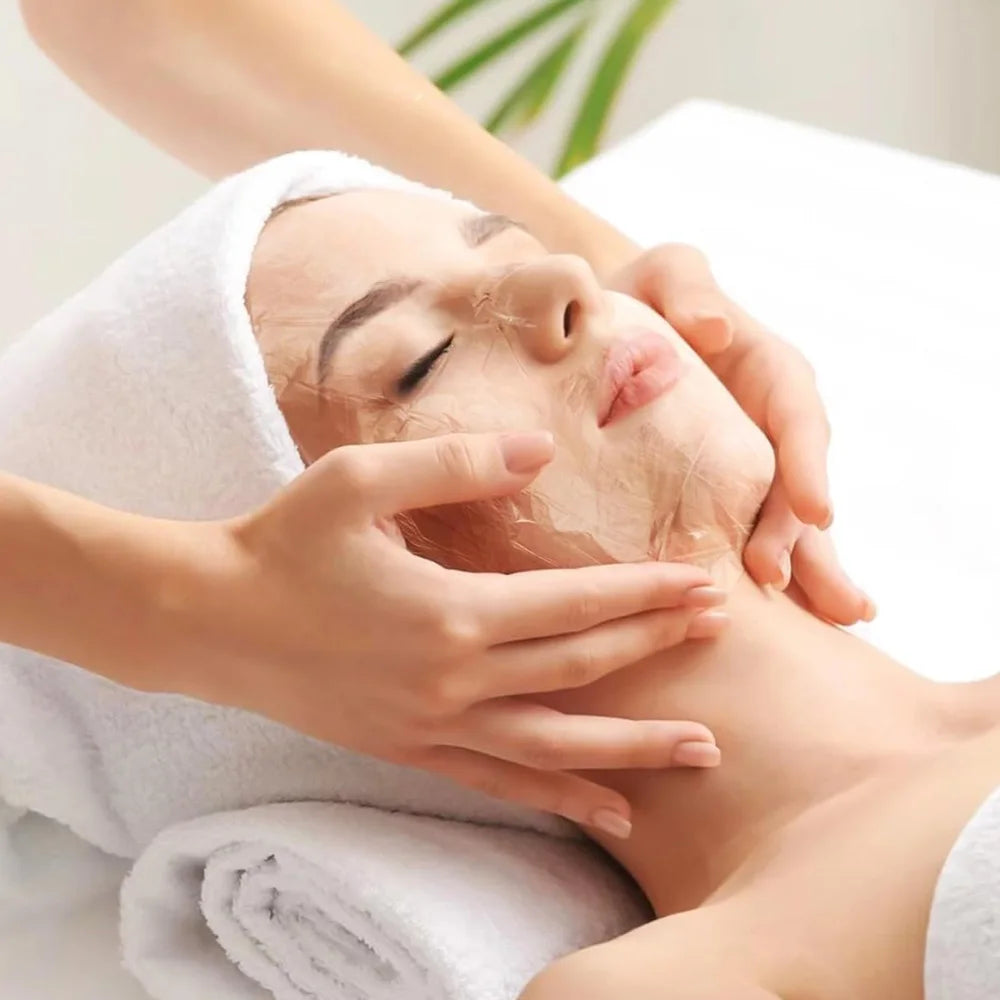A person receiving a spa facial treatment with a thin, clear, disposable plastic mask sheet applied to their face.