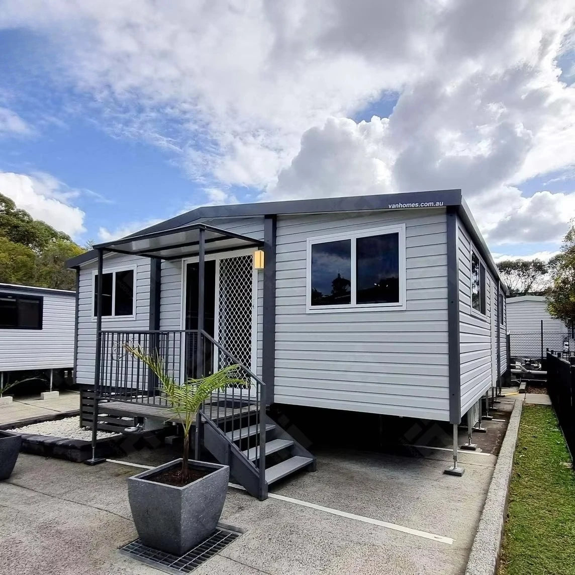 Gray modular container house with porch steps, railing, and large front window