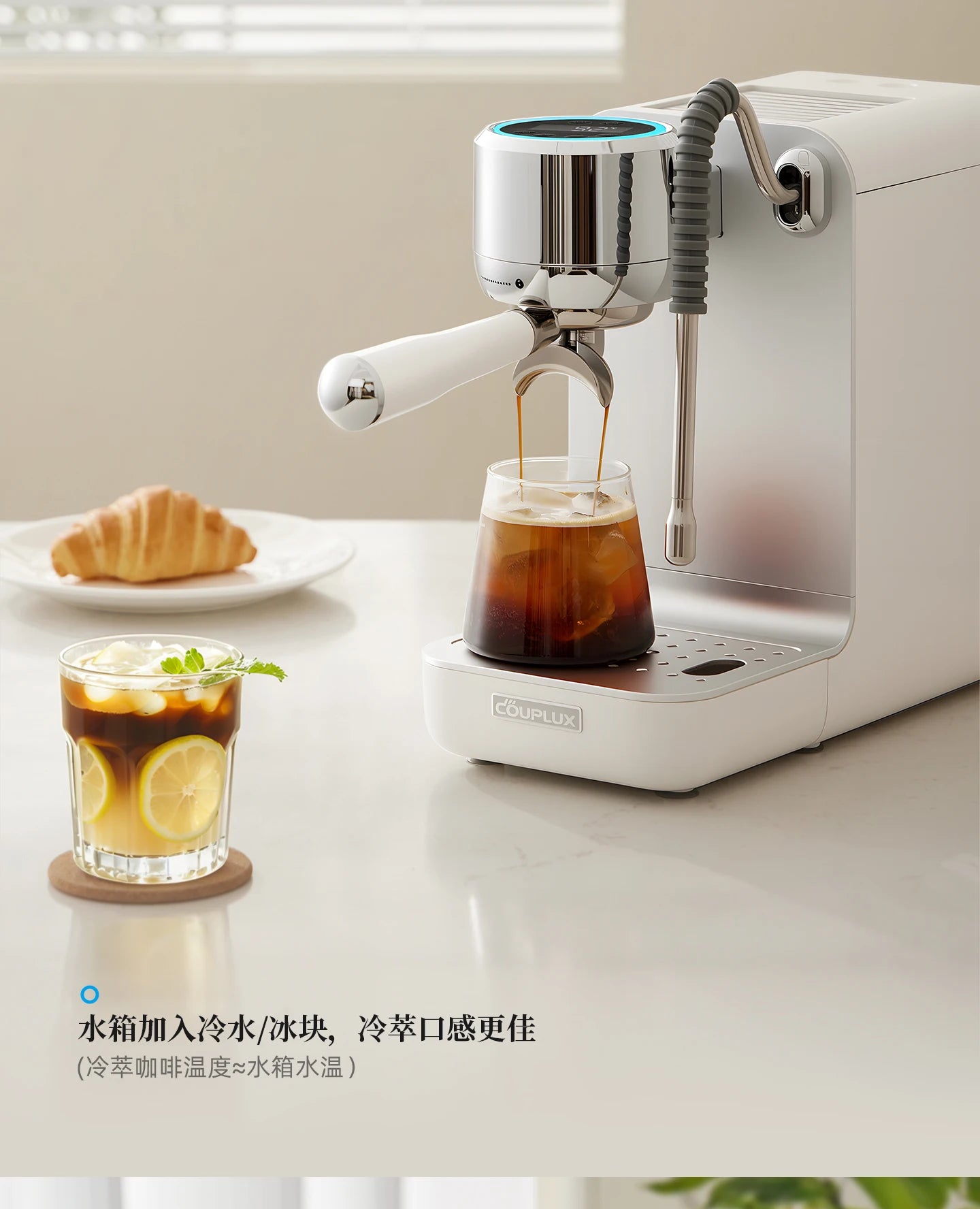 Couplux white compact espresso machine with silver accents brewing iced coffee into a glass on a modern kitchen counter.