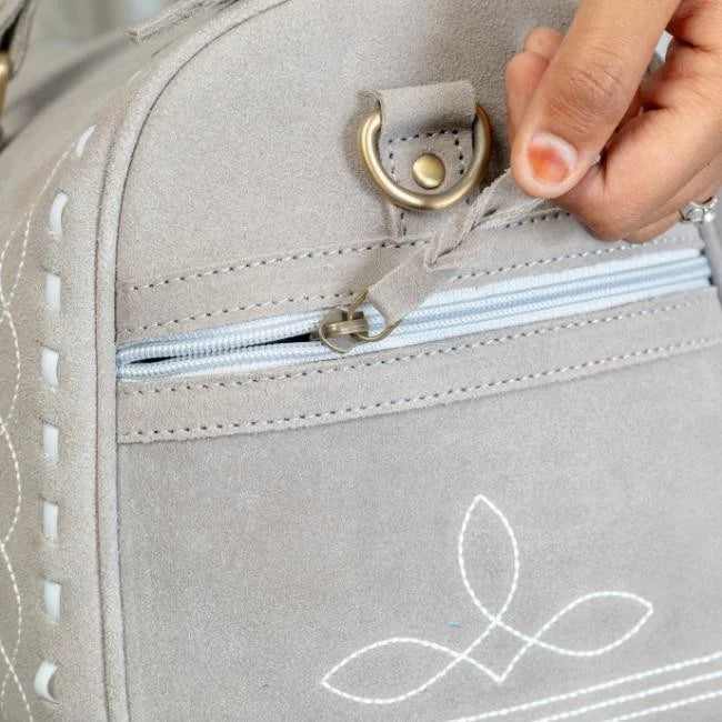 Grey suede leather weekend trunk bag with elegant white boot stitch detail, brass hardware, and zipper side pocket.