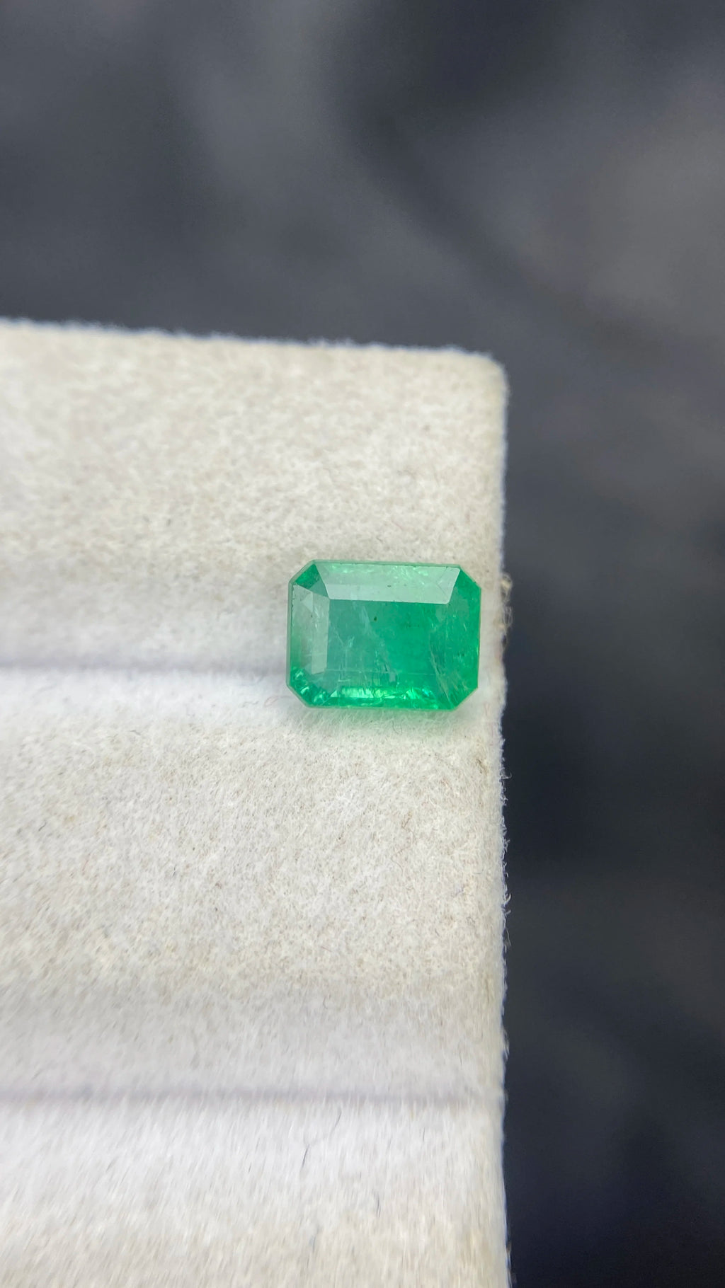 Green emerald-cut octagon gemstone on white cloth, close-up of angled facets