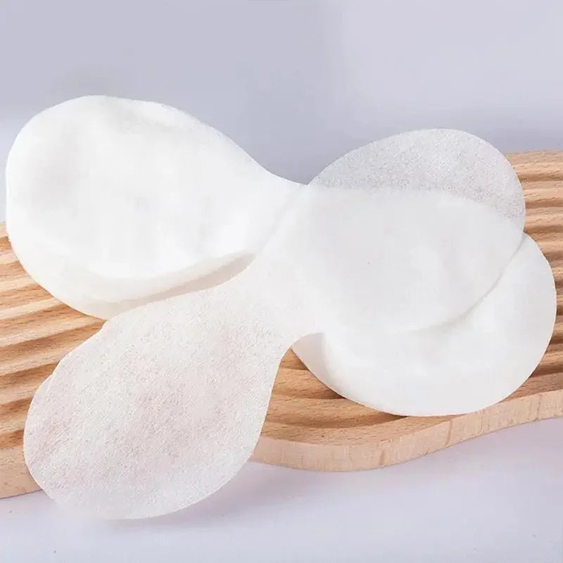 White, ultrathin disposable cotton eye mask papers shaped like petals, resting on a wooden ribbed surface.