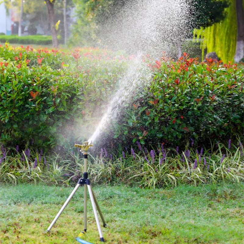 Rotating tripod sprinkler spraying fine mist over garden bushes and grass