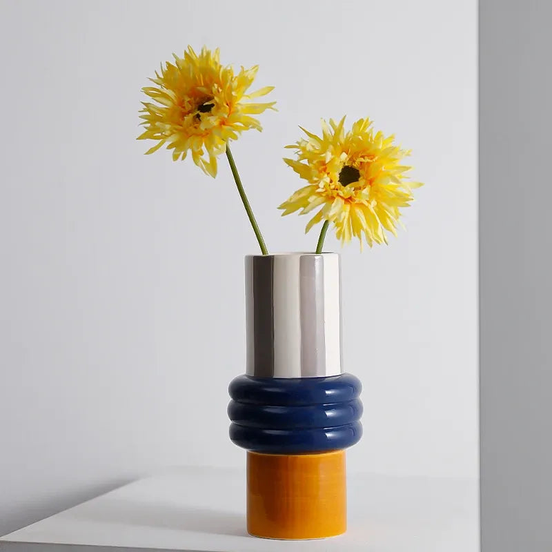 Ceramic vase with shiny silver top, blue ribbed neck, orange base holding yellow blooms