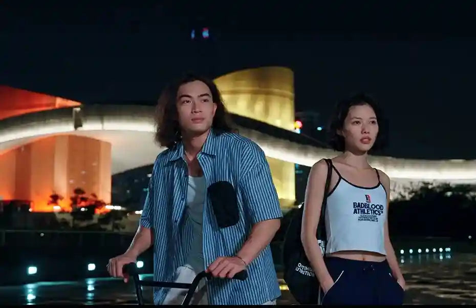 A man in a blue-and-white striped button-down shirt and a woman in a white tank top outdoors at night.