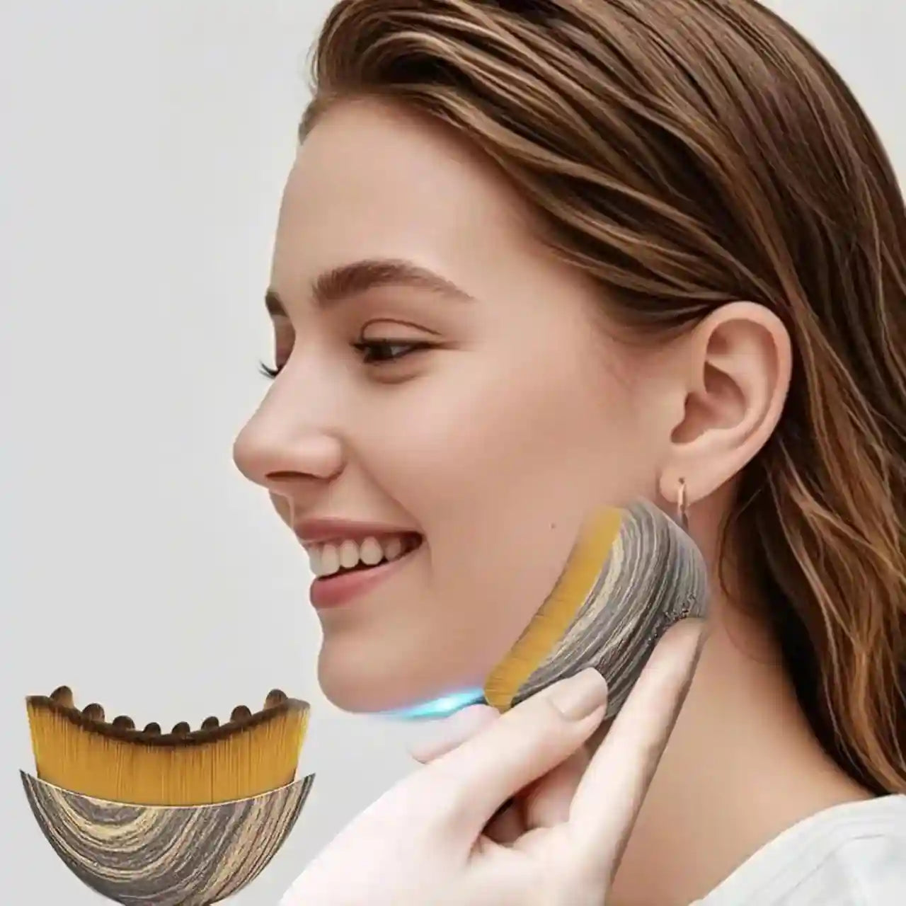 A person uses a wood-grain patterned, crescent-shaped facial massage brush with dense, yellow bristles on their jawline.