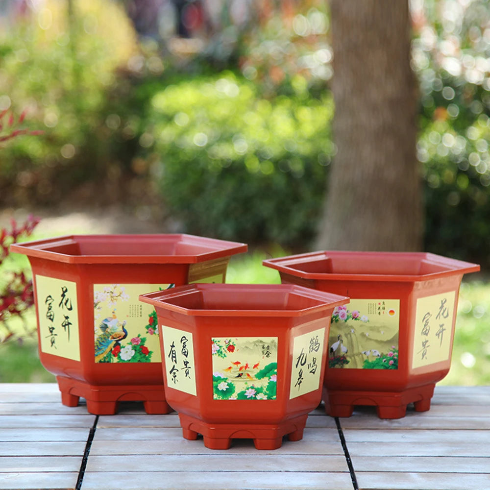 Set of three red illustrated resin flower pots with flared feet on a patio table.