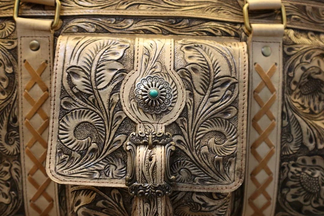 Vintage brown cowhide weekender duffel bag featuring ornate floral tooling, western carving, and a turquoise concho.