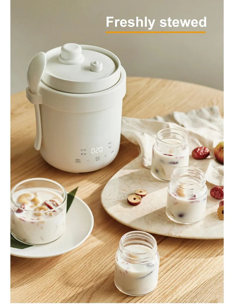 White mini electric stew pot with lid and carrying handle on wooden surface