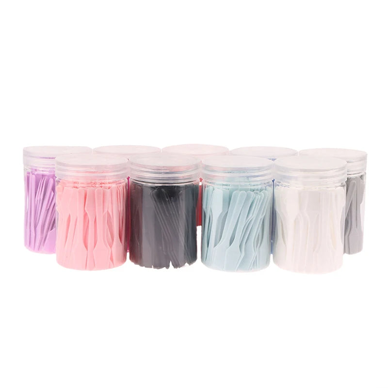 Several clear jars filled with small, colorful plastic cosmetic spatulas for face cream and makeup application.