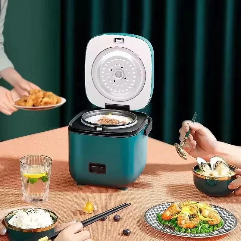 Mini electric rice cooker with teal body open lid, inner steam plate visible.