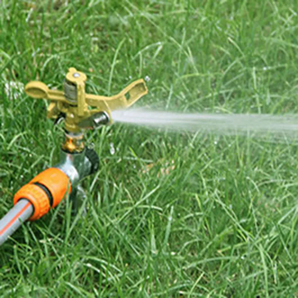 Hand using a gold garden sprinkler to spray water over green grass