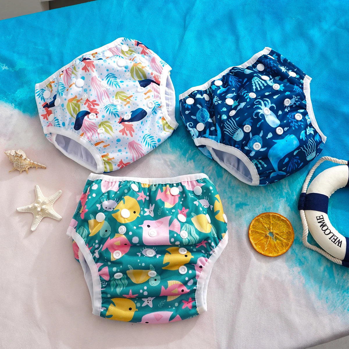 Three reusable baby swim diapers with cute nautical fish and ocean prints, adjustable snap design for infants.