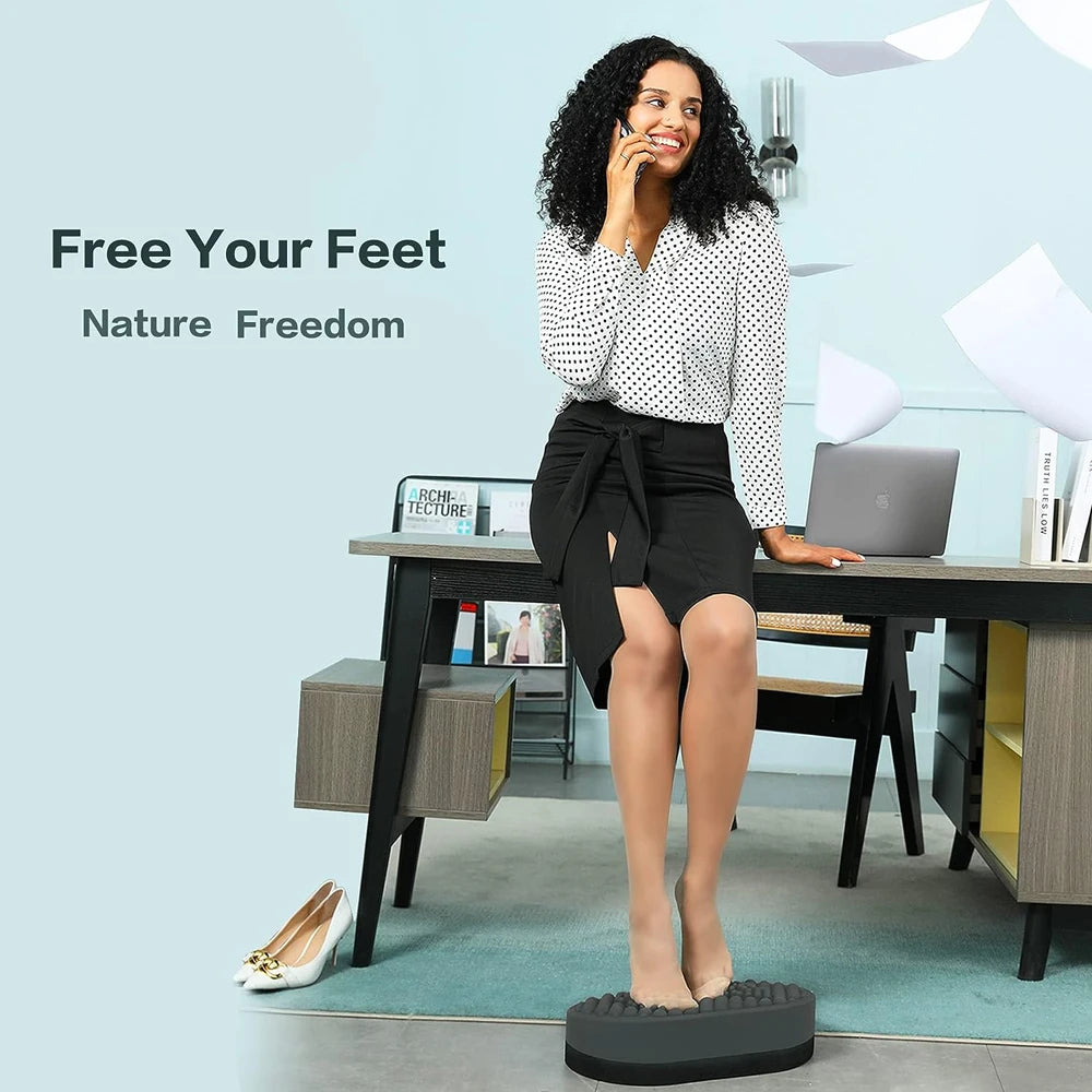 Woman using a gray ergonomic silicone foot massager stool for plantar fasciitis relief under a modern office desk.