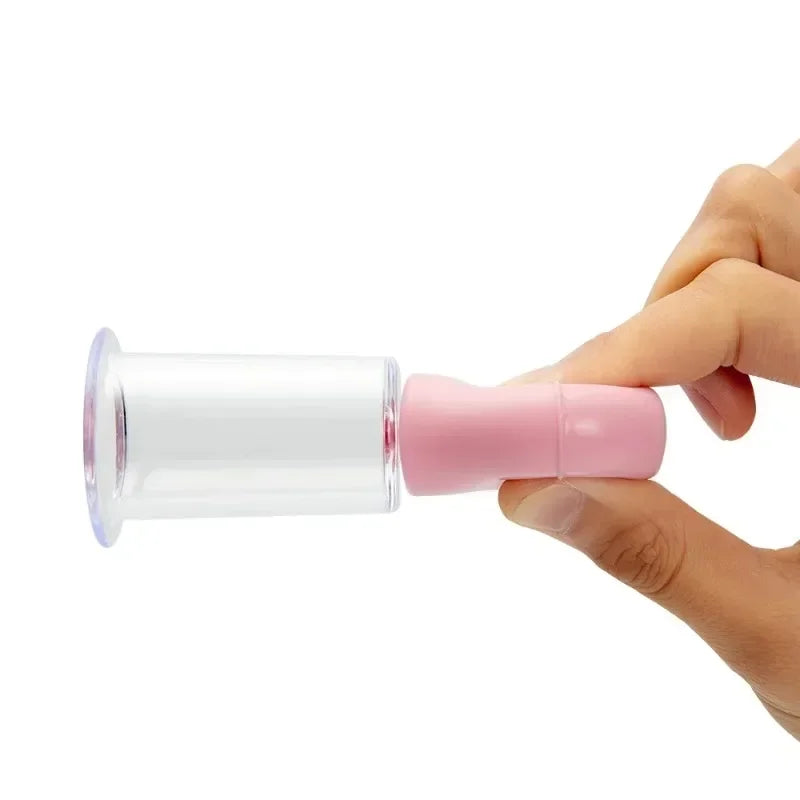 A hand holding a clear, cylindrical facial massage cupping tool with a pink rubber bulb, against a white background.