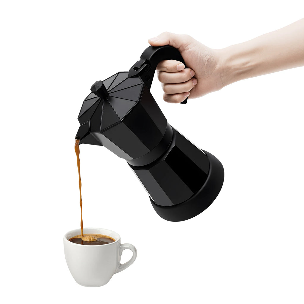 Hand pouring coffee from a modern matte black aluminum stovetop moka pot into a small white ceramic cup.