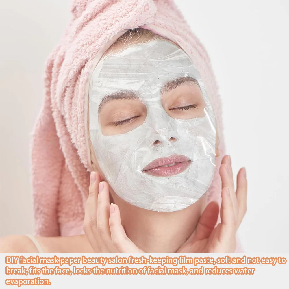 A woman in a pink towel wrap wears a transparent, thin plastic sheet facial mask over her skin with eyes closed.