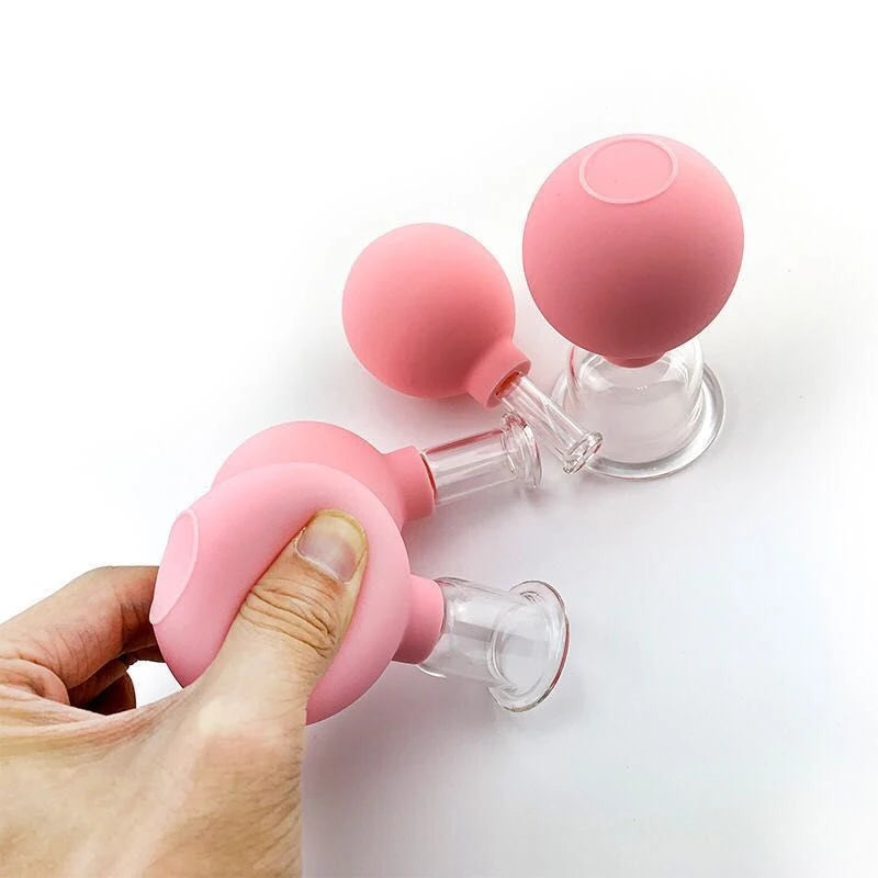 Three pink rubber and glass facial cupping tools on a white background, one held by a hand.