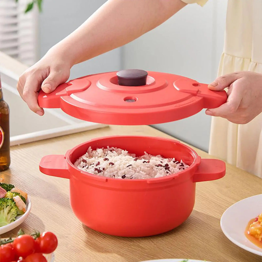 Red pressure cooker pot with lid lifted; rice inside on kitchen table.