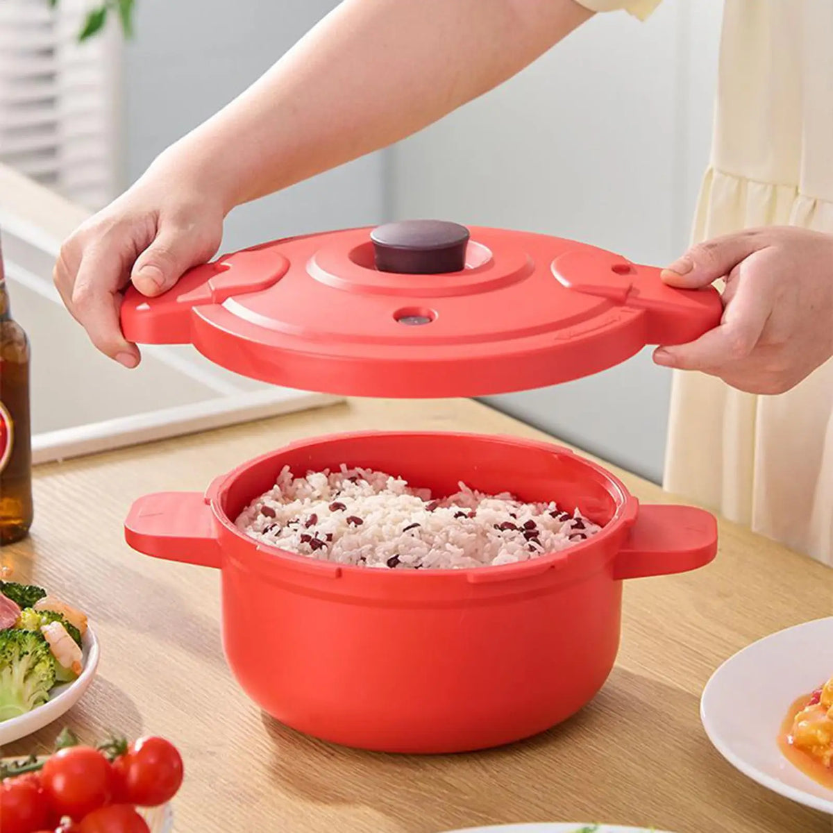 Red pressure cooker pot with lid lifted; rice inside on kitchen table.