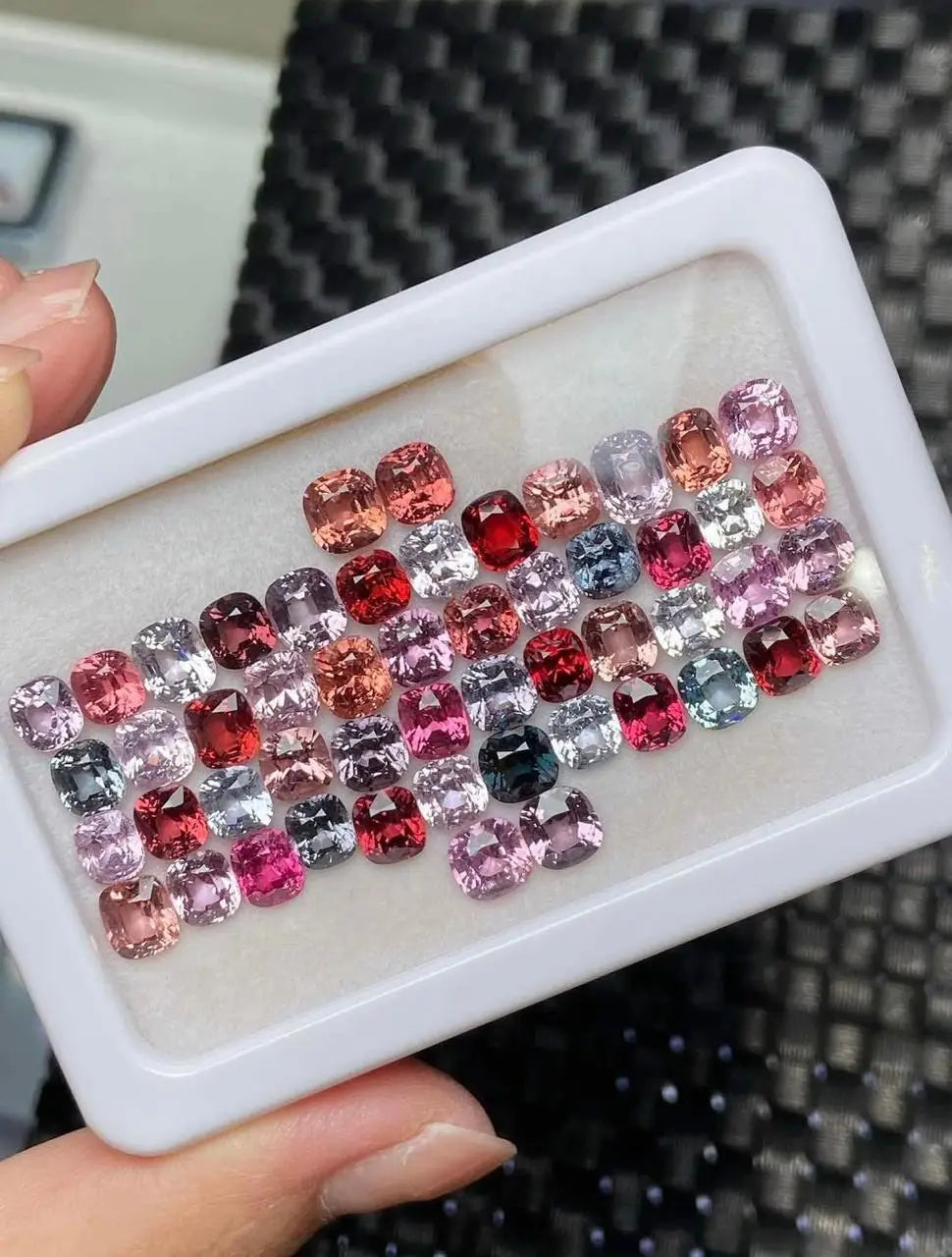 Loose gemstone set in white tray, featuring red, pink, purple, silver, and black stones