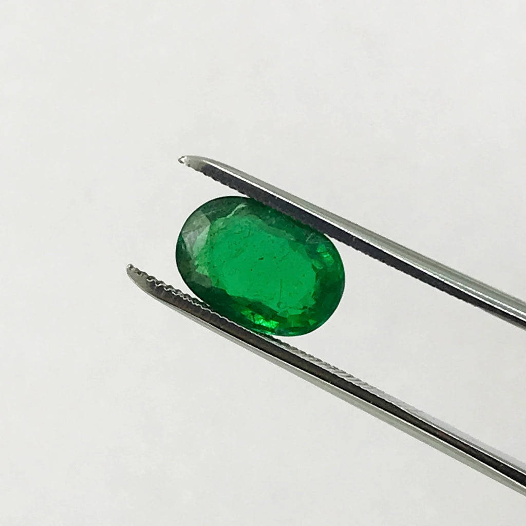 Green oval loose gemstone on metal tweezers, faceted sparkle