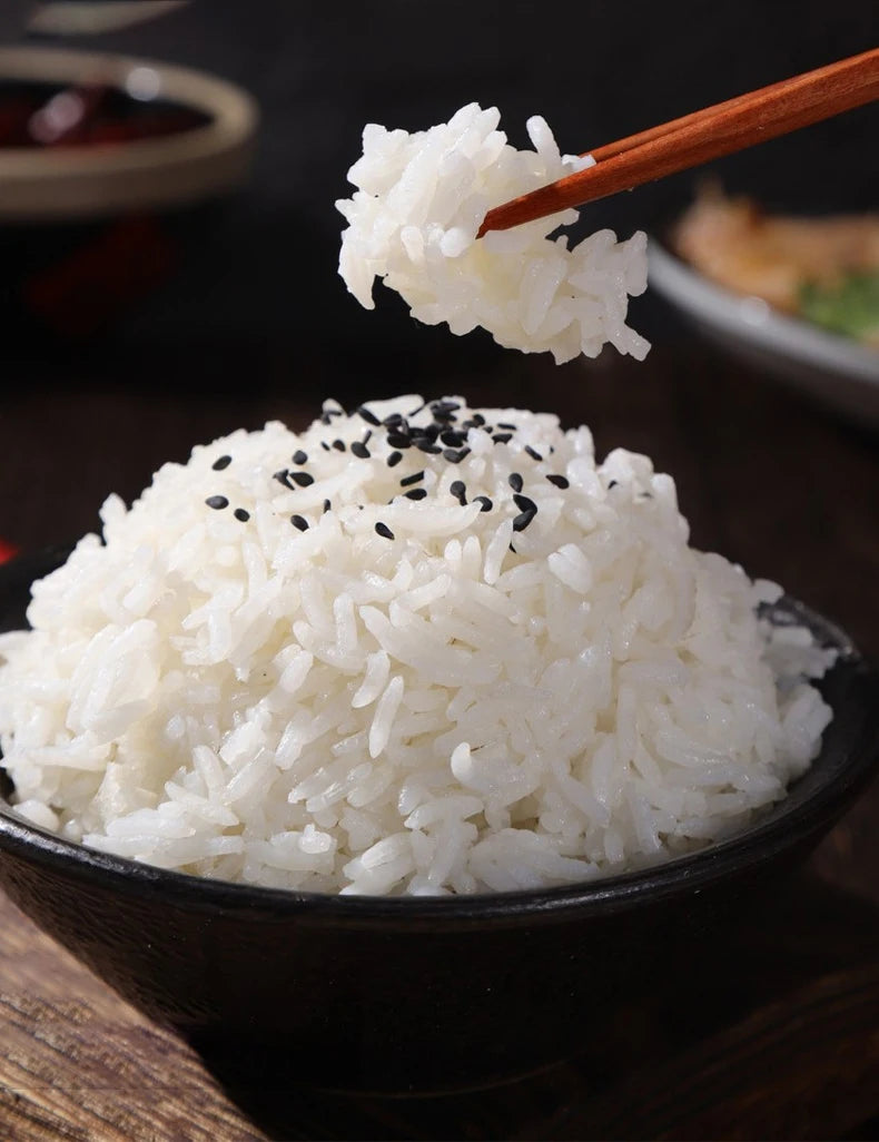 Bowl of steamed white rice with black seeds on dark background