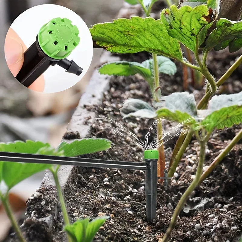 Green drip emitter on a black stake with water running onto garden soil