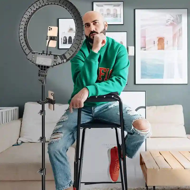 Large black circular LED ring light on a tall metal stand with integrated smartphone mounts for video content creation.