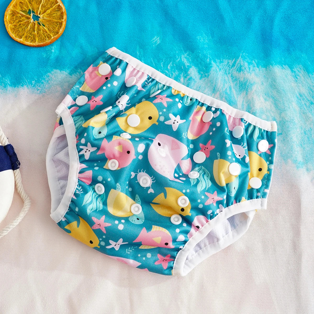Reusable cloth baby swim diaper with adjustable snaps, featuring colorful sea creature pattern on turquoise background.