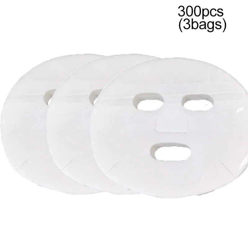 Three thin, white, circular disposable facial mask sheets with cutouts for eyes, nose, and mouth.