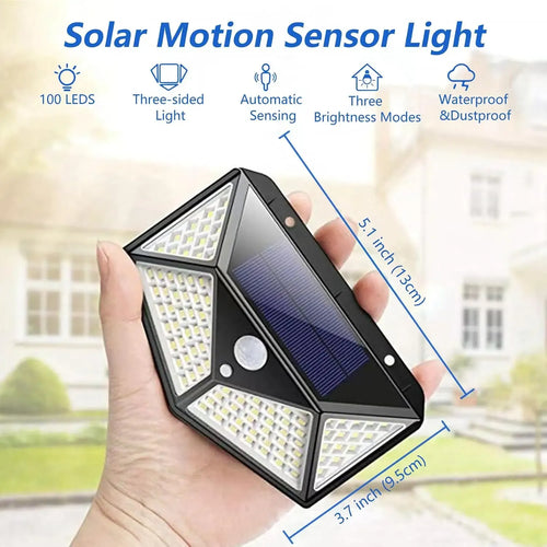 Black 100 LED solar wall light held in hand, featuring a central solar panel, motion sensor, and angled LED panels.