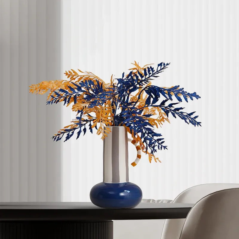 Ceramic vase with shiny silver top, blue neck, orange base, holding mixed dried leaves