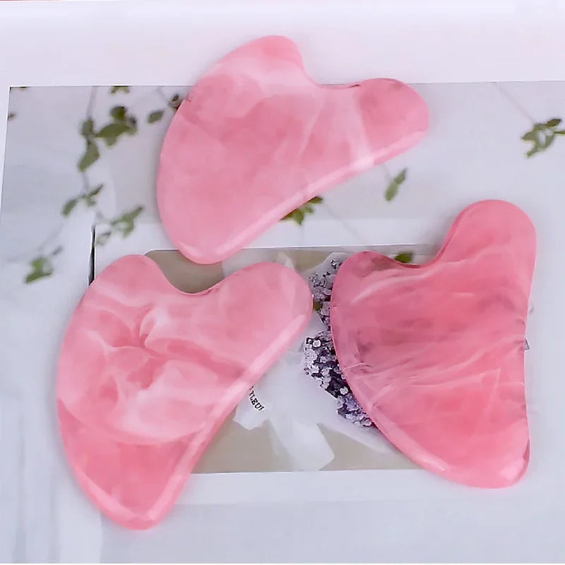 Three heart-shaped, pink marbled resin Gua Sha facial massage tools arranged on a white background.