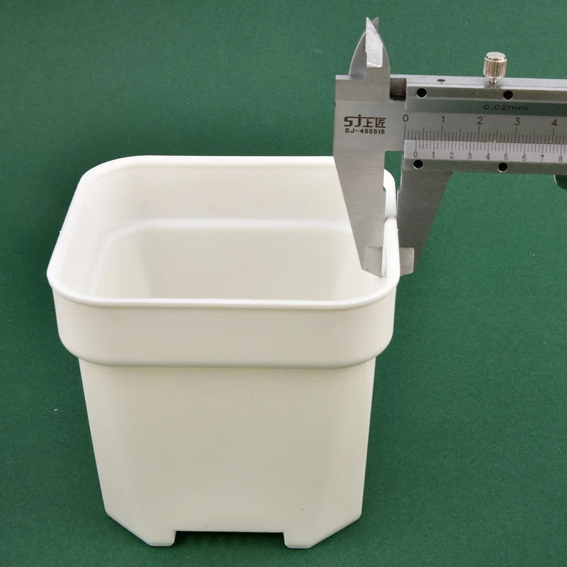 White square nursery planter pot with measuring caliper beside it