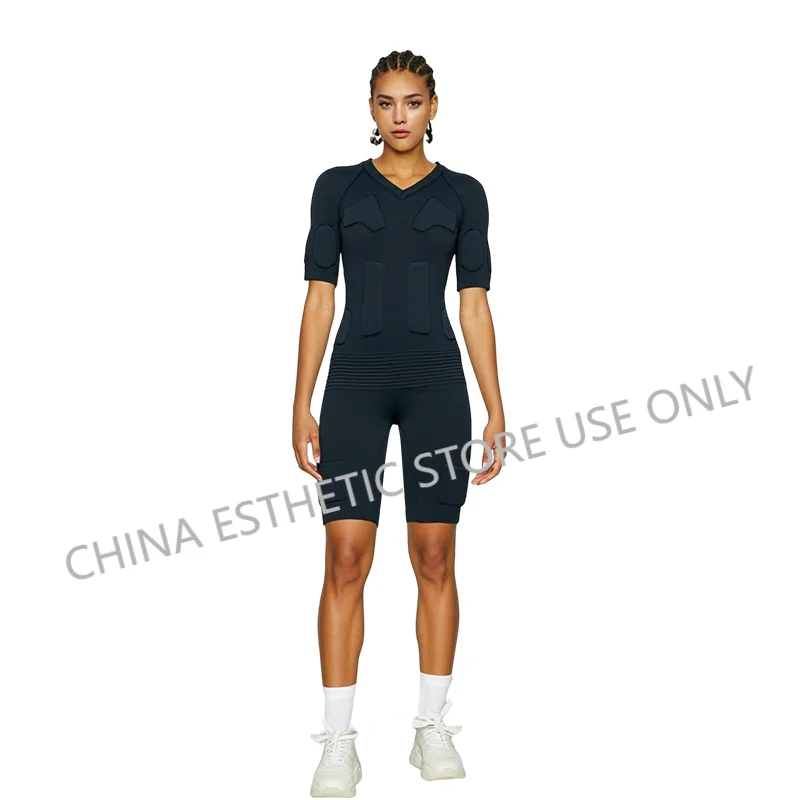 Woman wearing a black wireless EMS fitness suit with electrode pads for muscle training and home gym exercise.