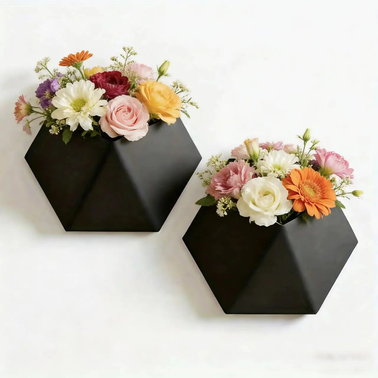 Black hexagonal wall planter with mounting holes, holding a floral bouquet