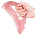 Hand holding a translucent, pink, S-shaped gua sha tool made of smooth resin for facial and body massage.