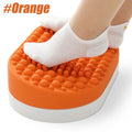 Orange silicone ergonomic under-desk foot rest with massage nodes for plantar fasciitis relief in a home office.