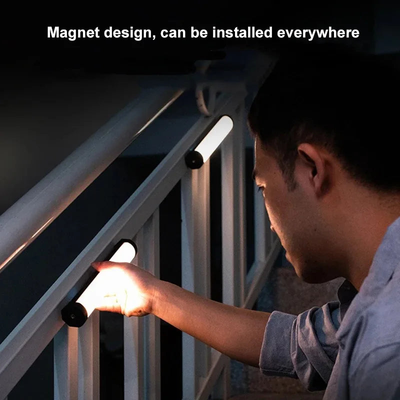 Magnetic, slim, cylindrical LED light bar emitting warm light, attached to a metal staircase railing.