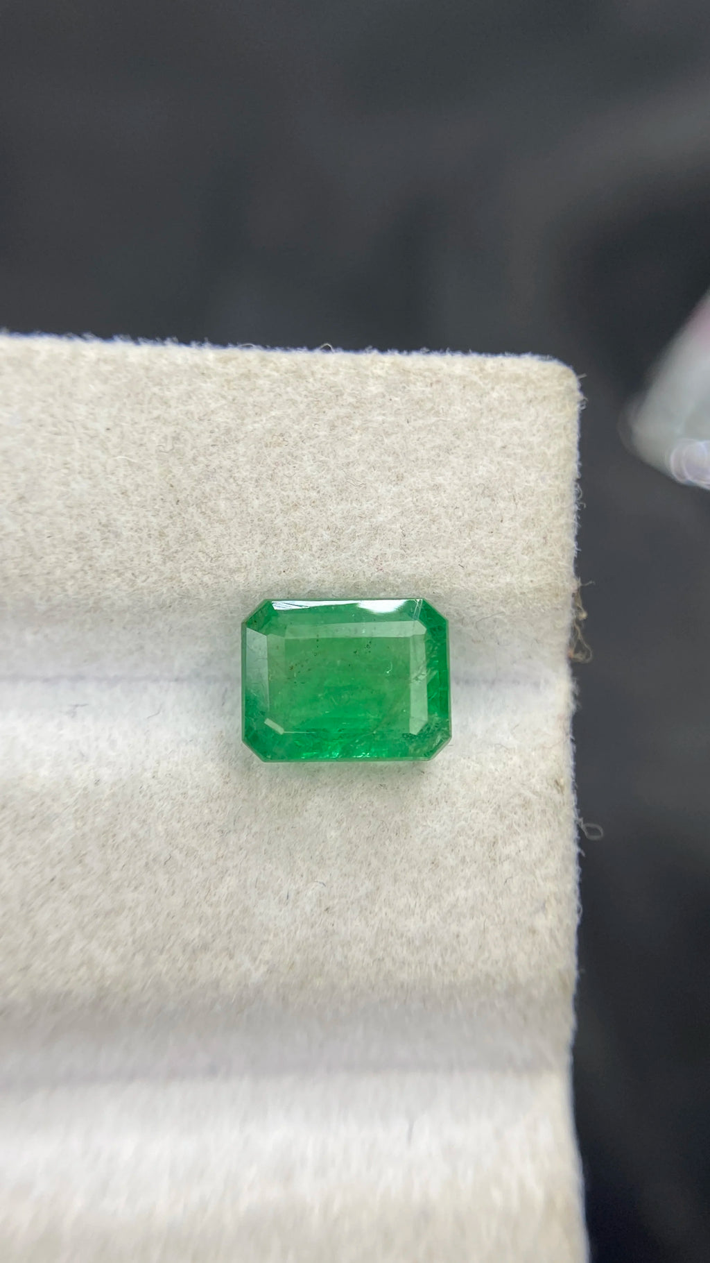 Green emerald-cut gemstone with octagon step facets on white velvet
