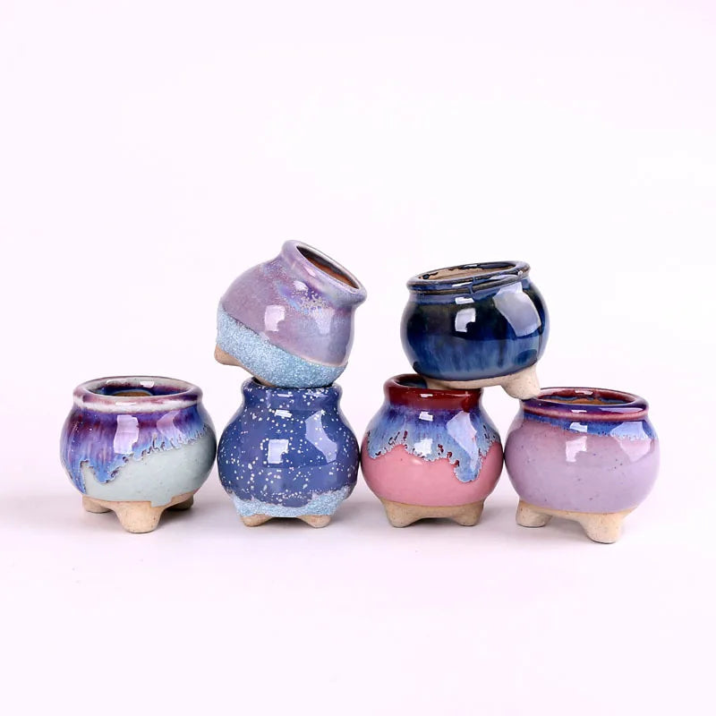 Five mini ceramic succulent pots in purple and blue tones, rounded with small tan feet