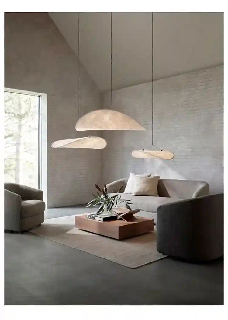 Three thin, cream-colored, organic-shaped pendant lights hanging above a modern living room sofa.