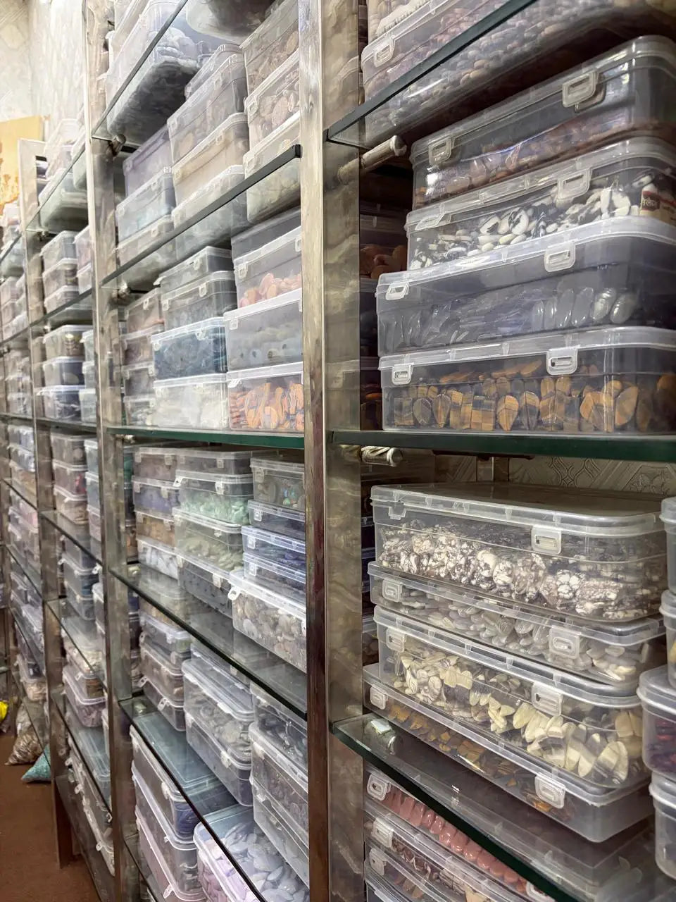 Rows of loose gemstones in clear plastic storage bins on shelves