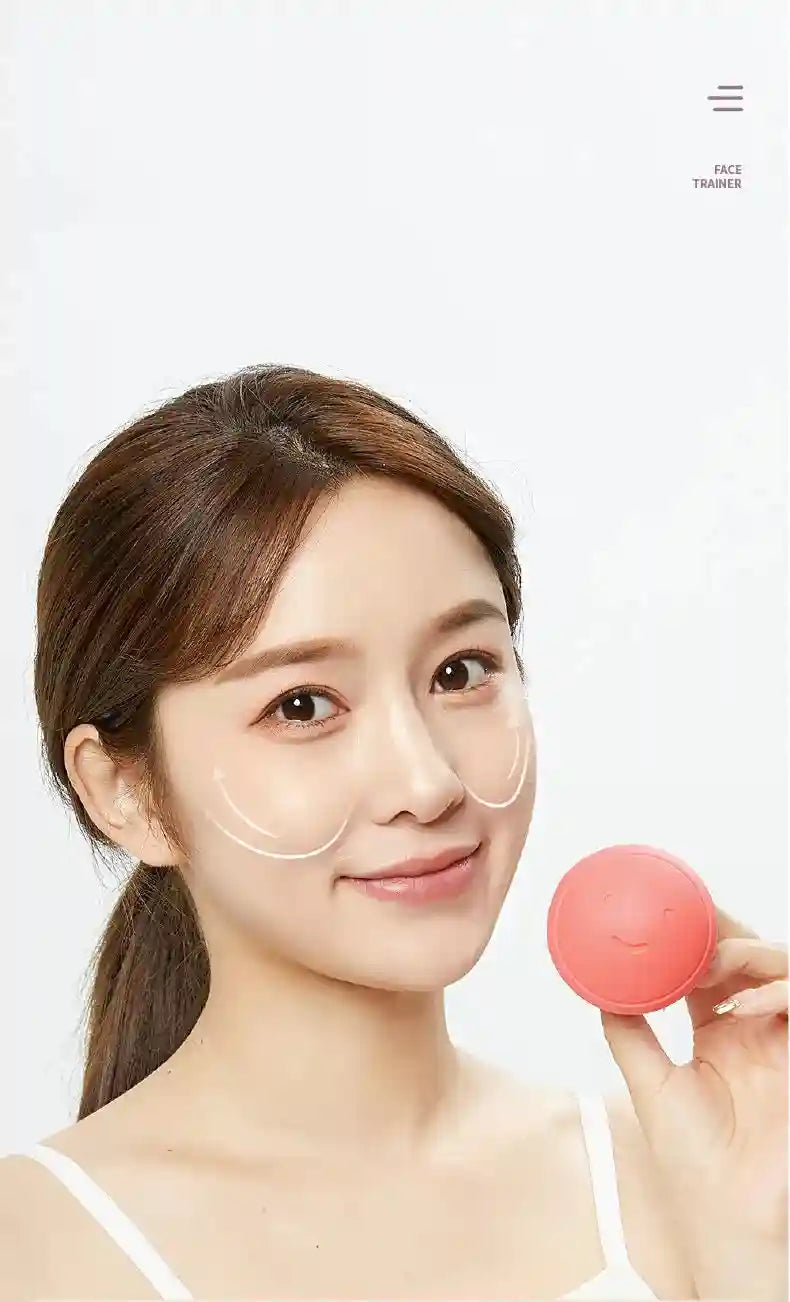 A woman holds a small, round, pink silicone face trainer tool with a smiling face design.