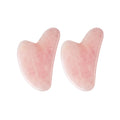 Two heart-shaped rose quartz gua sha facial massage tools with a smooth, polished light pink stone finish.