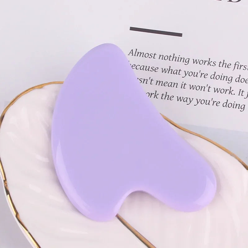 Smooth, light purple resin Gua Sha facial massage tool with a curved, multi-edged shape resting on a white tray.