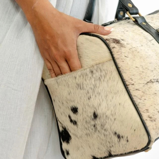 Unisex cow hair-on-hide weekender duffel bag with black leather trim, portable travel trunk style, side pocket.