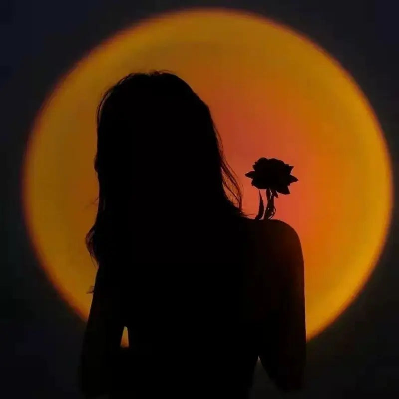 Sunset projection lamp creating a circular orange glow behind the silhouette of a woman holding a rose.